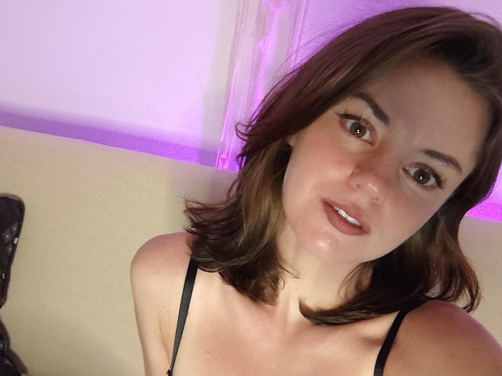 PamelaLogan with brown shoulder-length hair, black spaghetti strap top, light skin, brown eyes, slightly parted pink lips, and subtle makeup, looking at the camera.
