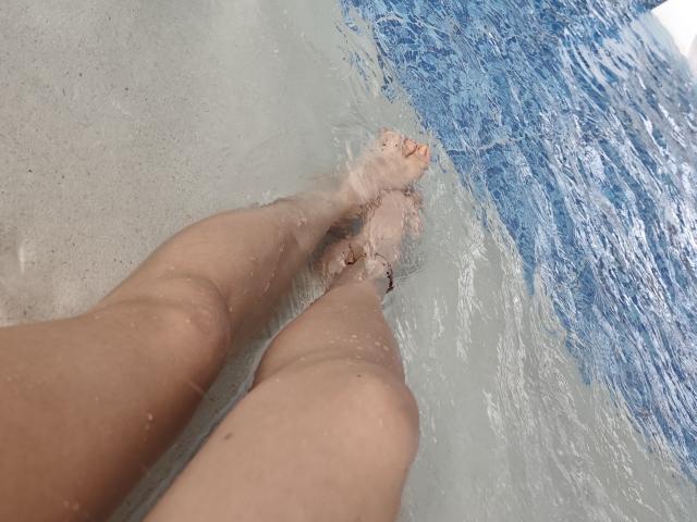 ScarlettAmelia's legs are in the water, with her toes slightly submerged. Her skin is tan, and there's a small brownish bug on her right ankle.