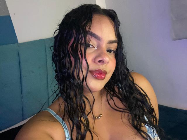 AmarantaCarey has wet, curly black hair, red lipstick, and a light blue bra. She's smiling with her eyes slightly closed, wearing a necklace with a small pendant.