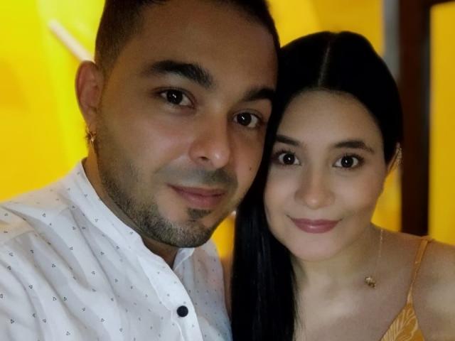 SwetShastity with short dark hair and light skin, wearing a white shirt with small patterns, and another SwetShastity with long black hair and light skin, in a yellow-lit room.