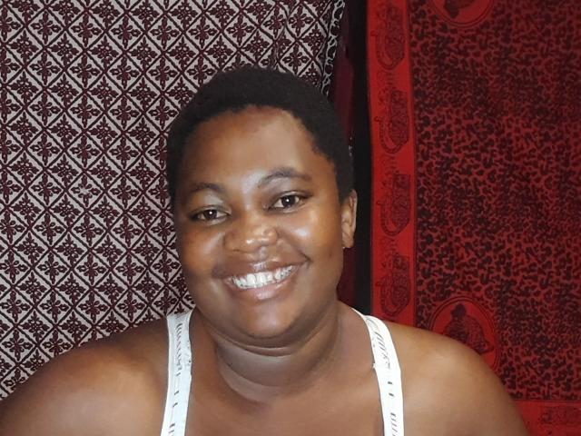 DoraKatty has dark brown skin, short black curly hair, and is smiling with teeth showing. She's wearing a white tank top, showing her small ass.