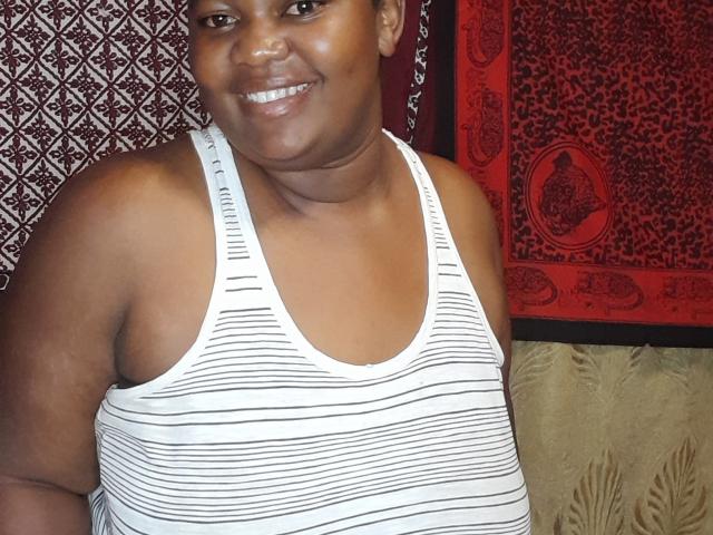 DoraKatty, a chubby black woman with brown skin and a smile, wearing a white and black striped tank top, showing her chubby arms and small tits.
