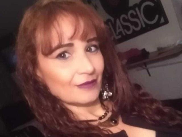 VictoriaLaRose has red curly hair, purple lipstick, and is wearing a black top with a beaded necklace. Her tits are small, and she's smiling slightly.