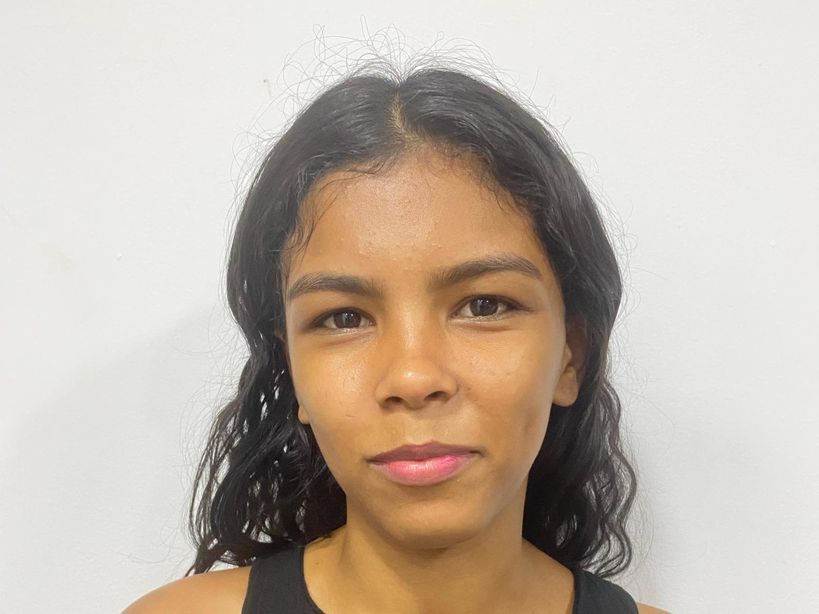 AngelsParadiise has medium brown skin, wavy black hair, brown eyes, and pink lipstick. She's wearing a black tank top with a neutral expression.