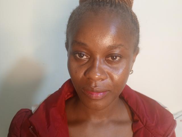 BrownieLush has dark brown skin, small earrings, a red jacket, and a slightly glossy face with a subtle frown. She's looking straight at the camera with a neutral expression.
