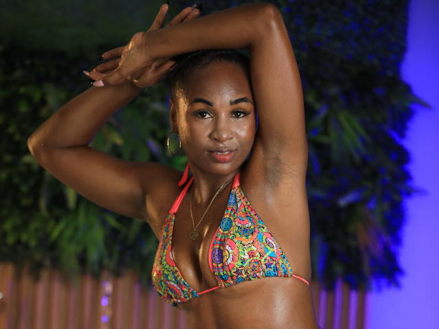 NathyRoss with dark skin, small colorful bikini, arms raised, showing armpits, looking at camera, gold hoop earrings, subtle smile, blue lighting in background.