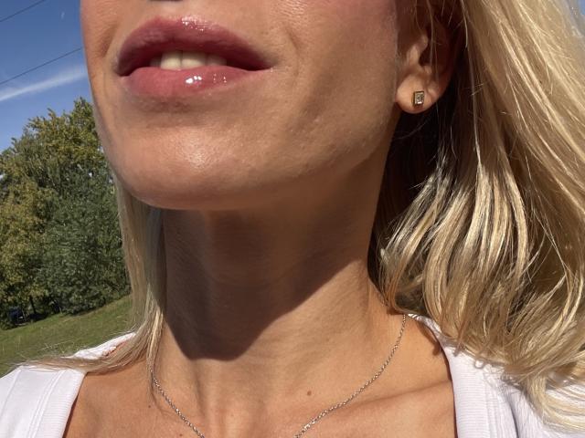 SandraSwweet's glossy pink lips, slightly parted, showing a bit of teeth. She has blonde hair, a small square earring, and a delicate silver necklace. Her neck is visible.