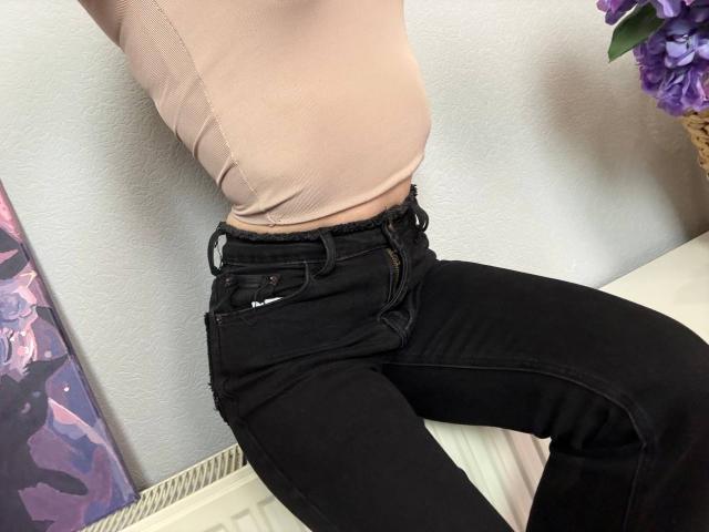 Amabel's tight pink top shows her small, rounded ass, while her black jeans sit low on her hips. Purple flowers in the background. Amabel's hands are out of frame.
