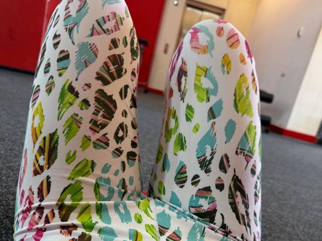 Amabel's colorful, patterned pants, featuring green, pink, blue, and black abstract shapes, are spread out on a gray carpet, with her white socks visible.