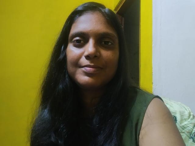 FlirtyAngel has long black hair, brown eyes, and a slight smile. She's wearing a green sleeveless top, looking directly at the camera. Her ass is not visible.