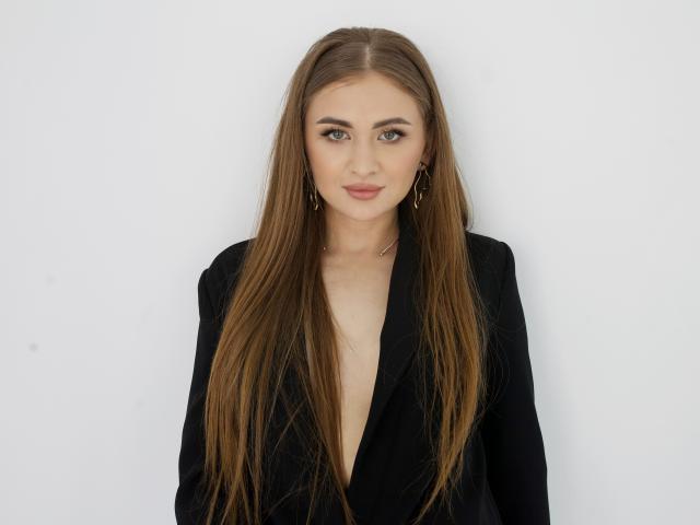 BeataAngel has long brown hair, wearing a black blazer with a deep V-neck, showing a hint of her tits. She's looking straight at the camera with a slight smile.