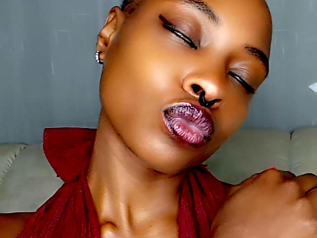 Queen-Adora-hot with shiny brown skin, closed eyes, and purple lipstick, wearing a red top, has a nose ring and small earrings, head tilted back, looking sexy.