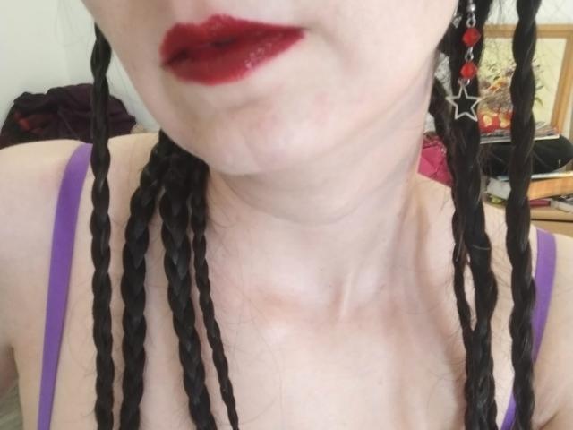  AlexandraSweet with dark red lipstick, braided black hair, and purple straps, showing pale skin and a slightly visible neck. Boobs partially visible, no other body parts shown.