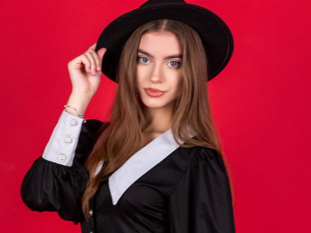 EricaDiaz with long brown hair, blue eyes, black hat, black dress with white collar, holding hat, red background, smiling, wearing bracelet, black dress, cute, sexy.