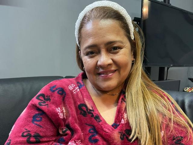 MonzerratBoyer with long blonde hair, white headband, pink patterned robe, smiling, showing small tits, sitting on black leather, looking at camera, medium skin, slight wrinkles, casual photo.
