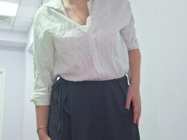 Triziya wearing a white button-up shirt and black skirt, her right hand in her pocket, with a bracelet on her wrist and black nail polish.
