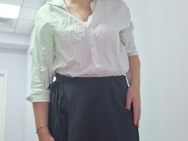 Triziya with pale skin, white button-up shirt, black skirt, and black nail polish, standing, head not visible, right hand in skirt pocket, left wrist with bracelet.