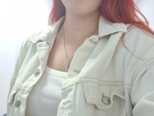 Triziya's pale green jacket, open to show white ribbed top, small silver necklace with 'L' pendant, red hair, no visible tits or ass, soft light, casual look.