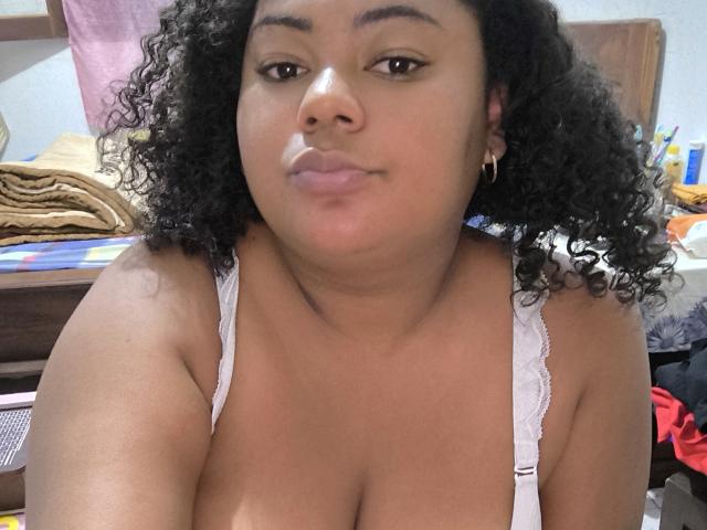 WendyStar69 has dark curly hair, brown skin, and is wearing a white lace bra, showing her big tits and puffy lips in a selfie. She's looking at the camera.
