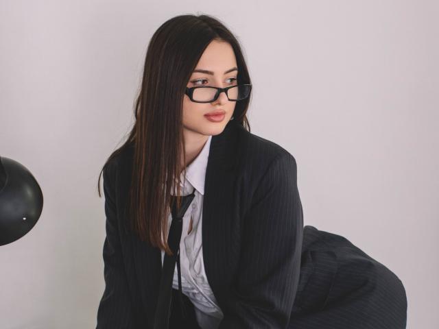 ChristinaBliss with long brown hair, glasses, and a pinstripe suit, leaning forward, showing her ass, wearing a white shirt and black tie, looking over her shoulder.