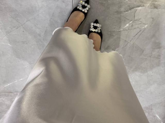 Amabel's legs in a white dress, showing her black pointed shoes with diamond-shaped studs. Her feet are slightly apart, standing on a marble floor.