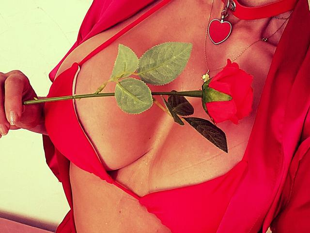 De rode bikini-top van LaParisienne bedekt nauwelijks haar grote borsten, en ze houdt een rode roos tussen hen. Ze draagt een rode hart-ketting, met een open rood shirt..