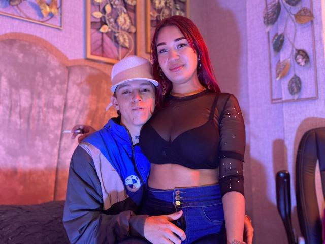 PhoenixEvelyn with tits in a black bra, standing next to a dude in a white hat and blue jacket, holding a soccer ball, in a dimly lit room.