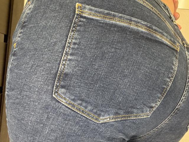 Barbarica's denim ass, showing a tight, blue, back pocket with yellow stitching, emphasizing her round, full butt. The texture is slightly worn, highlighting her curves.