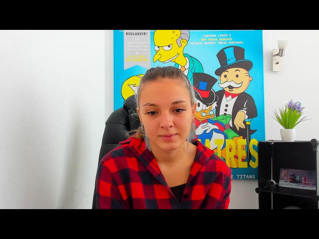 Melilla with puffy brown face, blonde ponytail, and red-black checkered robe, sitting in front of Simpsons poster, looking bored. She has small tits and a cute face.