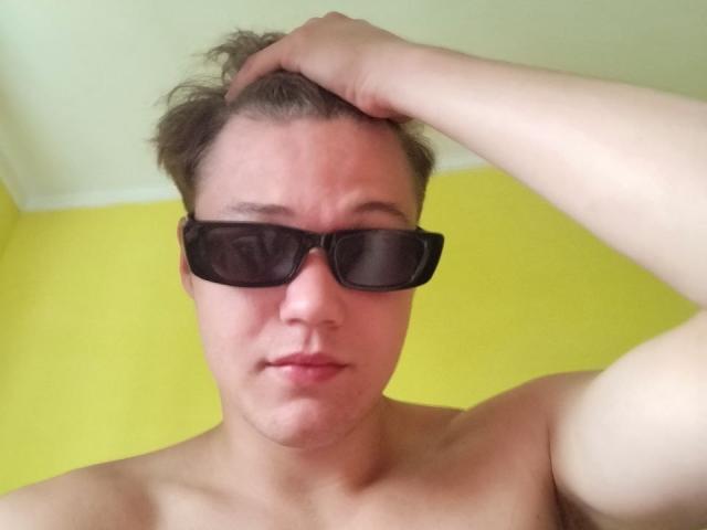 LucasLong with short brown hair, wearing black sunglasses, shirtless, and hand in hair, has a slightly annoyed or confused expression. His ass is not visible.