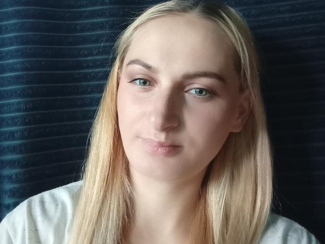 ForestCandyX a les cheveux blonds, les yeux verts et un léger sourire. Elle porte une chemise blanche, et son visage est au centre de l'image. Ses seins sont petits et mignons..
