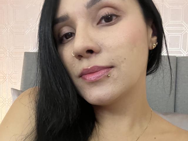YessiJaymes has black hair, brown eyes, a nose ring, gold earrings, a lip piercing, and a small beauty mark below her right eye. Her skin is light and smooth.