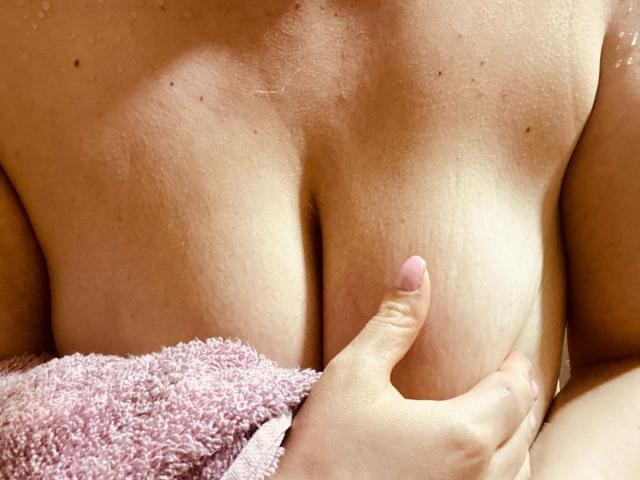 I seni di CocoVolkov, tenuti dalla sua stessa mano, con un asciugamano rosa che copre la parte inferiore del suo corpo, mostrando la sua pelle chiara e i piccoli capezzoli rotondi..