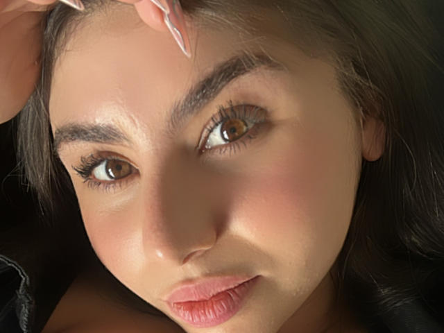 Het gezicht van VenusxMusa, bruine ogen, lange wimpers, licht open roze lippen, hand die het hoofd aanraakt, donkerbruin haar, lichte huid, subtiele blos, zacht licht, geconcentreerde uitdrukking, close-up..