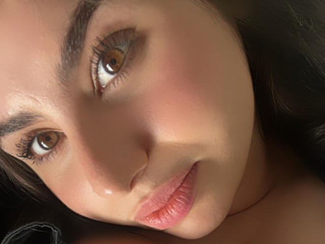 VenusxMusa ha gli occhi marrone chiaro, labbra piene rosate e un leggero sorriso. È sdraiata, con i capelli castano scuro, la pelle chiara e un leggero alone sul viso..