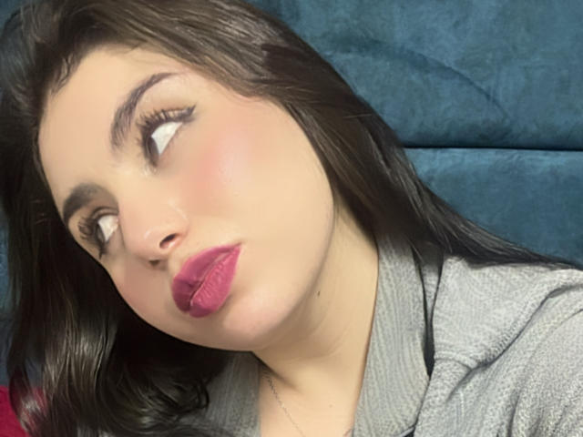 VenusxMusa, avec des lèvres roses et gonflées, un nez légèrement retroussé et des yeux marron qui regardent sur le côté. Elle a de longs cheveux noirs et porte un sweat à capuche gris..