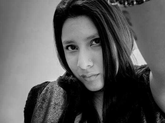 Black-and-white photo of LadyStarOne with medium-length dark hair, nose piercing, and soft smile. She's wearing a textured, dark sleeveless top, with a slightly blurred background.