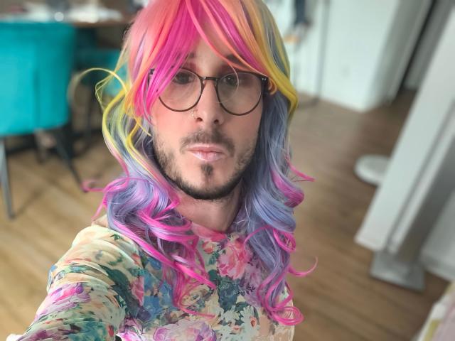 GingerPink-hot with colorful rainbow hair, glasses, and beard, wearing a floral shirt, showing a neutral facial expression, in a selfie. Boob-free, pussy-free, ass-free.