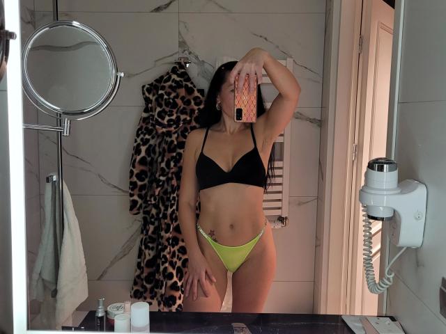 SweetJolina-hot wearing black bra and yellow-green panties, holding phone covering face, leopard robe hanging, white towel, marble wall, mirror reflection, black countertop with toiletries.