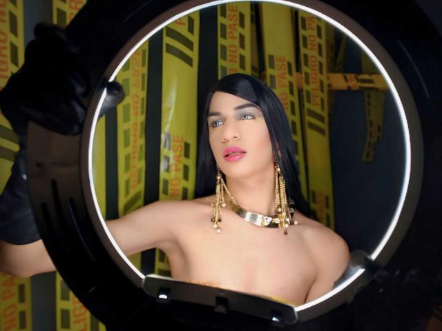KendallSky with black hair, wearing gold earrings and a silver necklace, topless, looking through a circular ring light, black gloves, pink lipstick, and a cute expression.