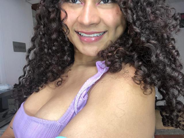 LalilaBrunette with dark hair, white face mask, white bandeau top, white shorts, blue star hair clip, sitting on teal velvet couch, showing her small tits and flat ass.