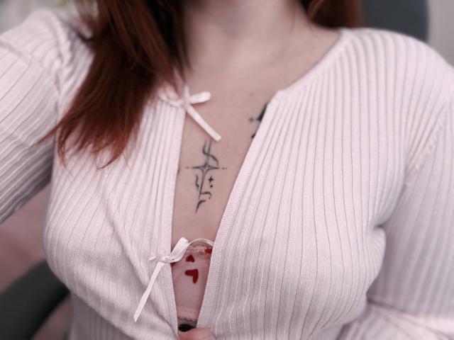 I seni di Rubbi sono coperti da una camicia rosa a coste con bottoni, leggermente aperta per rivelare un tatuaggio a forma di stella nera e dei segni a forma di cuore rossi sul suo petto..