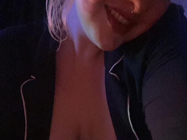 CocoVolkov's face with a smile, showing a nose ring, and wearing an open black top, exposing a bit of cleavage. Her lips are slightly parted.