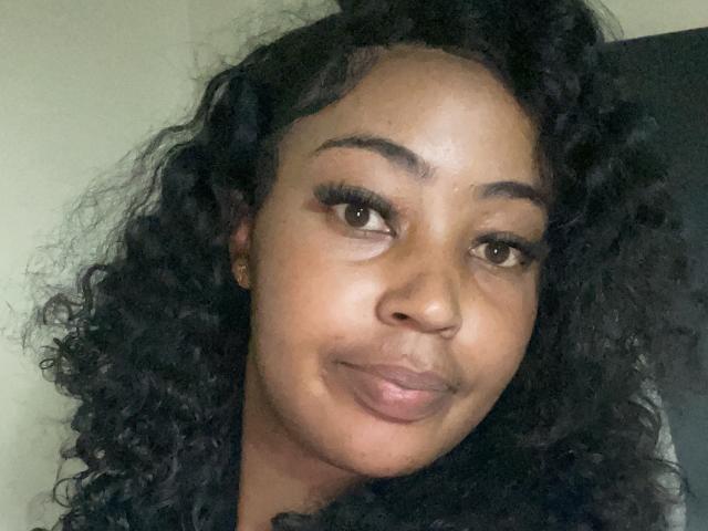 PreatyLexxi has curly black hair, brown eyes, and a slight smile. Her nose is flat and her lips are full. She's wearing small gold earrings.