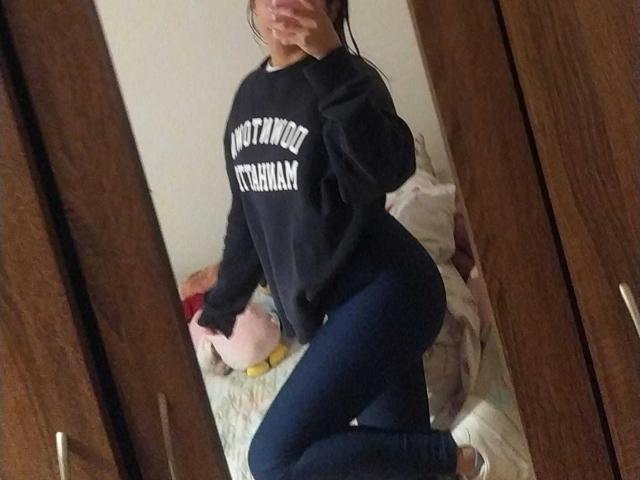 TinyLaurent in a black sweatshirt and tight blue jeans, kneeling in front of a mirror, showing her curvy ass and slim waist, with her face partially covered.