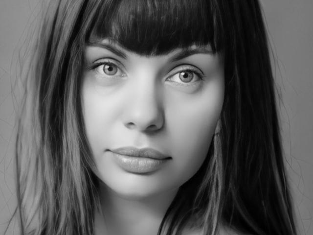 MalayaMe with dark, straight hair, wearing a denim jacket, rests her chin on her hand, looking straight into the camera, in a black-and-white shot. Her tits are small.