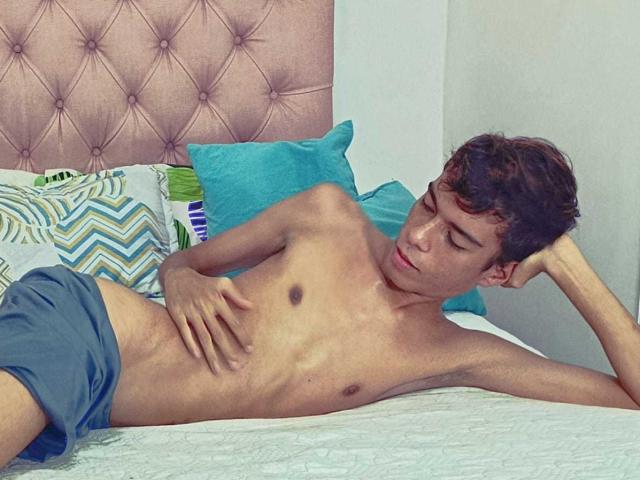 MaxSweett, a slim young dude with short brown hair, lying on a bed, shirtless, wearing blue shorts, hand on his flat chest, eyes closed, arm behind his head.
