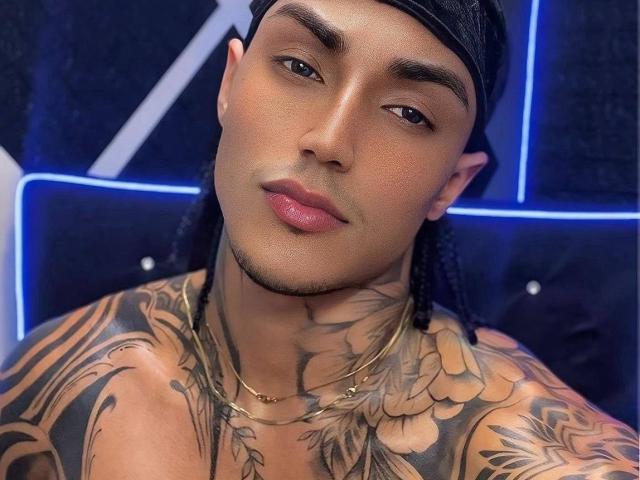 JarrodHaywardSex with a sexy tan face, black braided hair, and full lips, showing off extensive tattoos on his chest and neck, wearing a gold necklace, and looking at the camera.