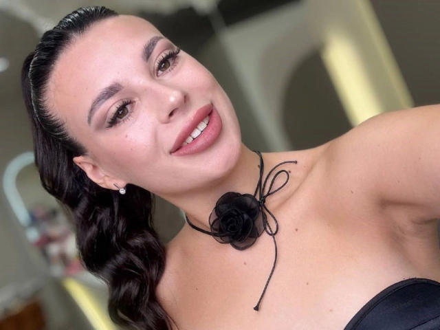 MoonriseGoddessx-hot with dark hair in a braid, smiling, wearing a black strapless top, black rose choker, and earrings, showing her tits and looking hot.