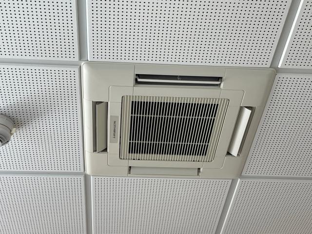 Grey ceiling vent with vertical slats, set in a perforated white tile panel. A white circular pipe is on the left. CatwalkStar-hot's ass up here, in a way.
